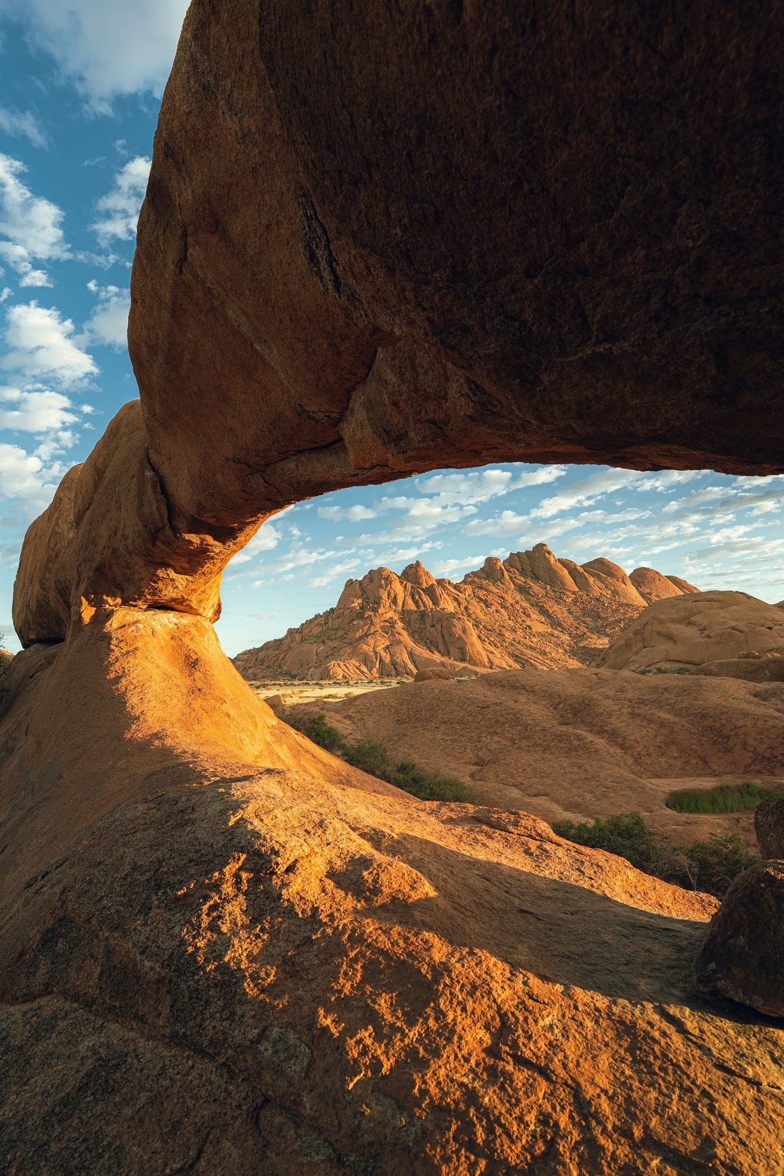 Natural rock arch framing desert mountains under a blue sky in Namibia
